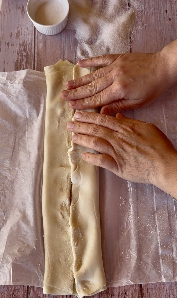 Lámina de hojaldre rectangular extendida sobre una superficie cubierta de azúcar blanco, lista para ser enrollada.