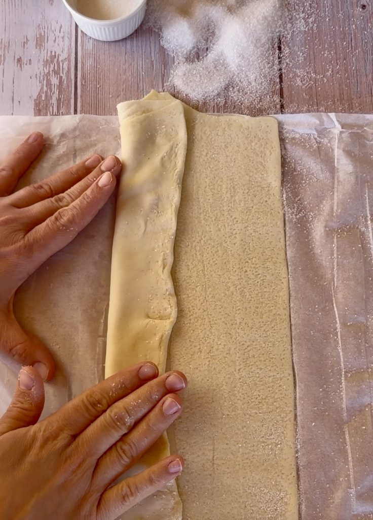 Lámina de hojaldre rectangular extendida sobre una superficie cubierta de azúcar blanco, lista para ser enrollada.