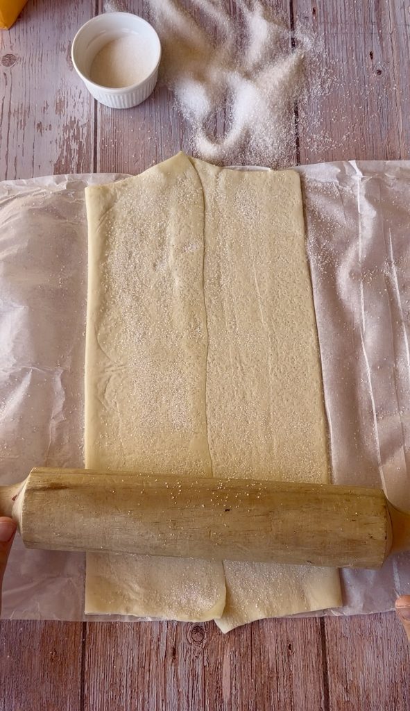 Lámina de hojaldre rectangular extendida sobre una superficie cubierta de azúcar blanco, lista para ser enrollada.