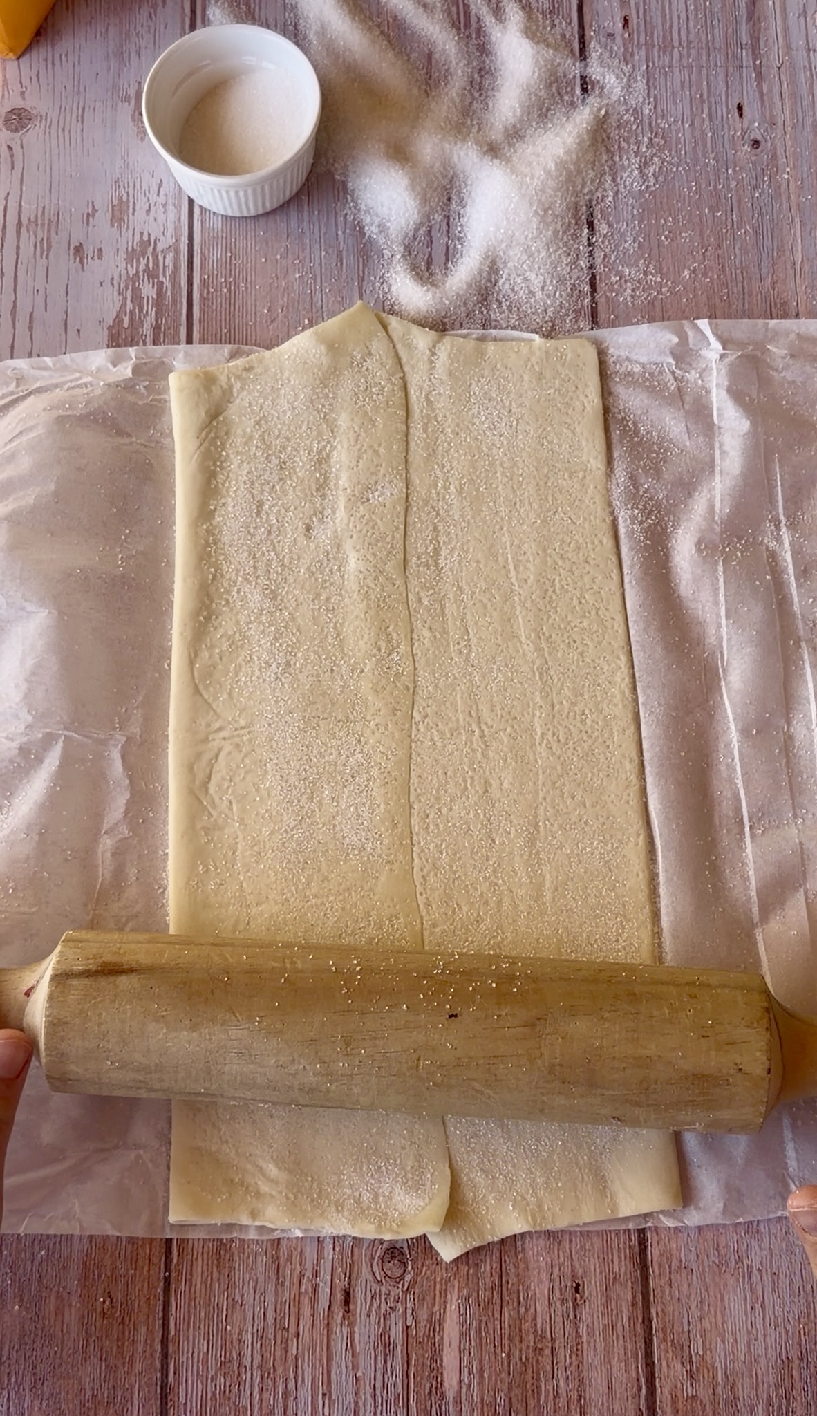 Lámina de hojaldre rectangular extendida sobre una superficie cubierta de azúcar blanco, lista para ser enrollada.