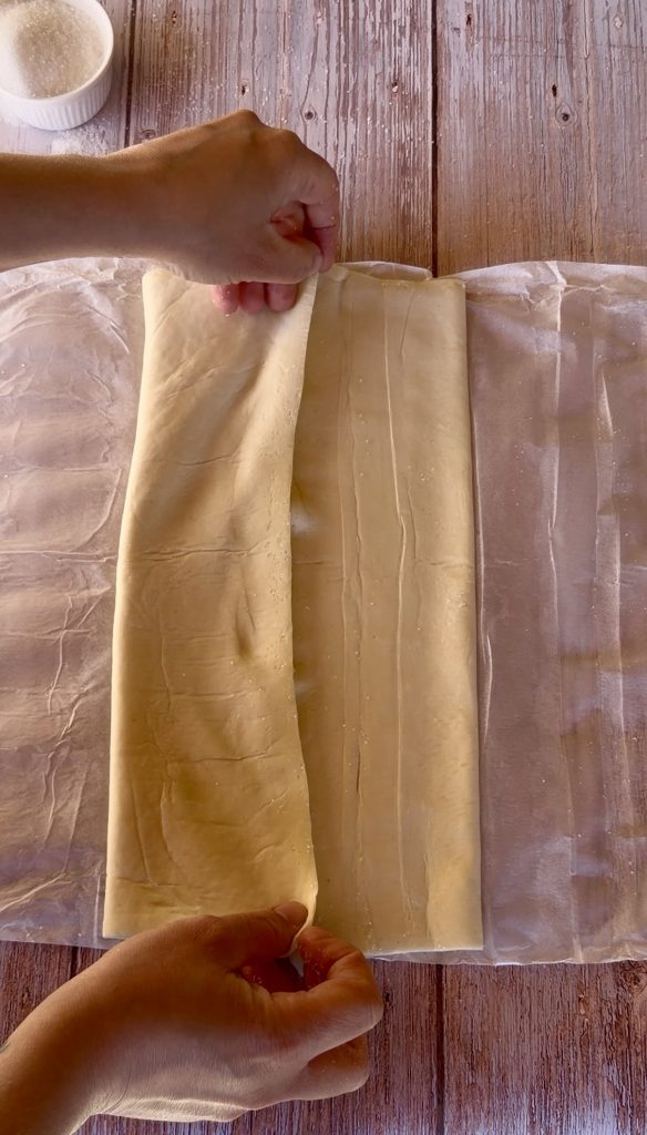 Lámina de hojaldre rectangular extendida sobre una superficie cubierta de azúcar blanco, lista para ser enrollada.