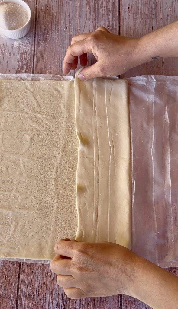 Lámina de hojaldre rectangular extendida sobre una superficie cubierta de azúcar blanco, lista para ser enrollada.