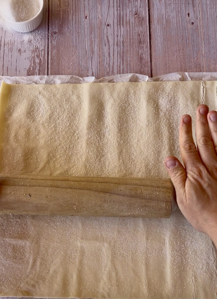 Lámina de hojaldre rectangular extendida sobre una superficie cubierta de azúcar blanco, lista para ser enrollada.