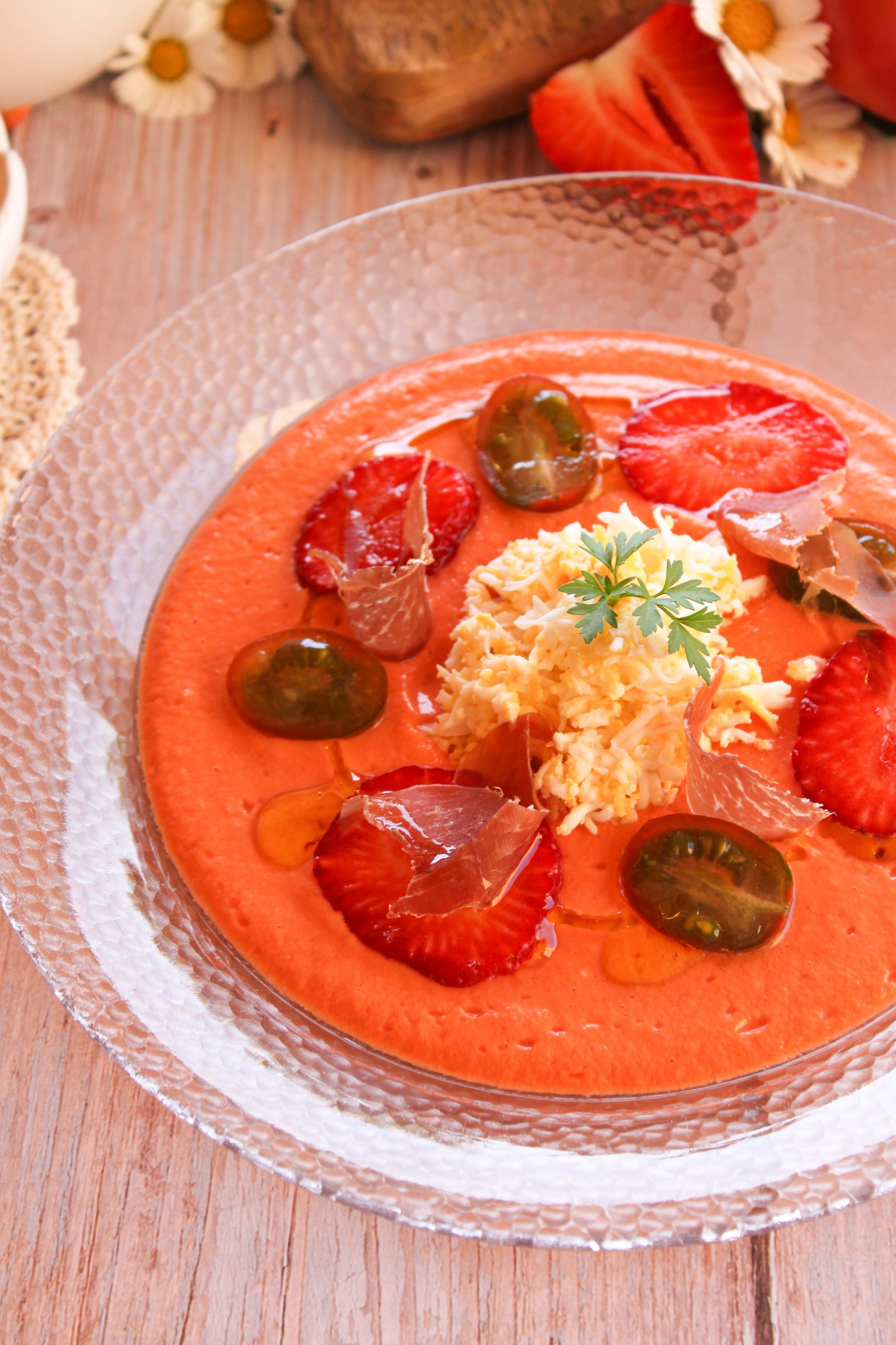 Cuenco rústico de salmorejo de fresas decorado con huevo duro rallado, jamón ibérico, tomates cherry y láminas de fresa.