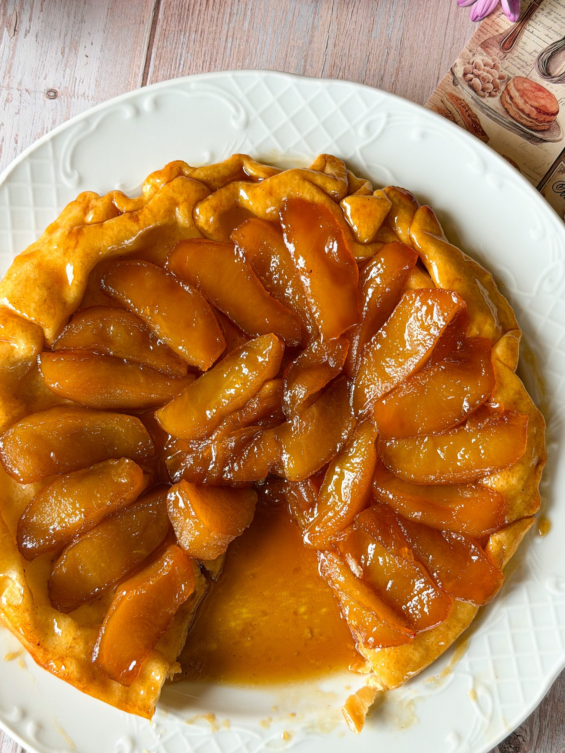 Tarta Tatin de manzana recién desmoldada en un plato blanco labrado, mostrando los gajos de manzana brillantes y bañados en un caramelo ambarino profundo.