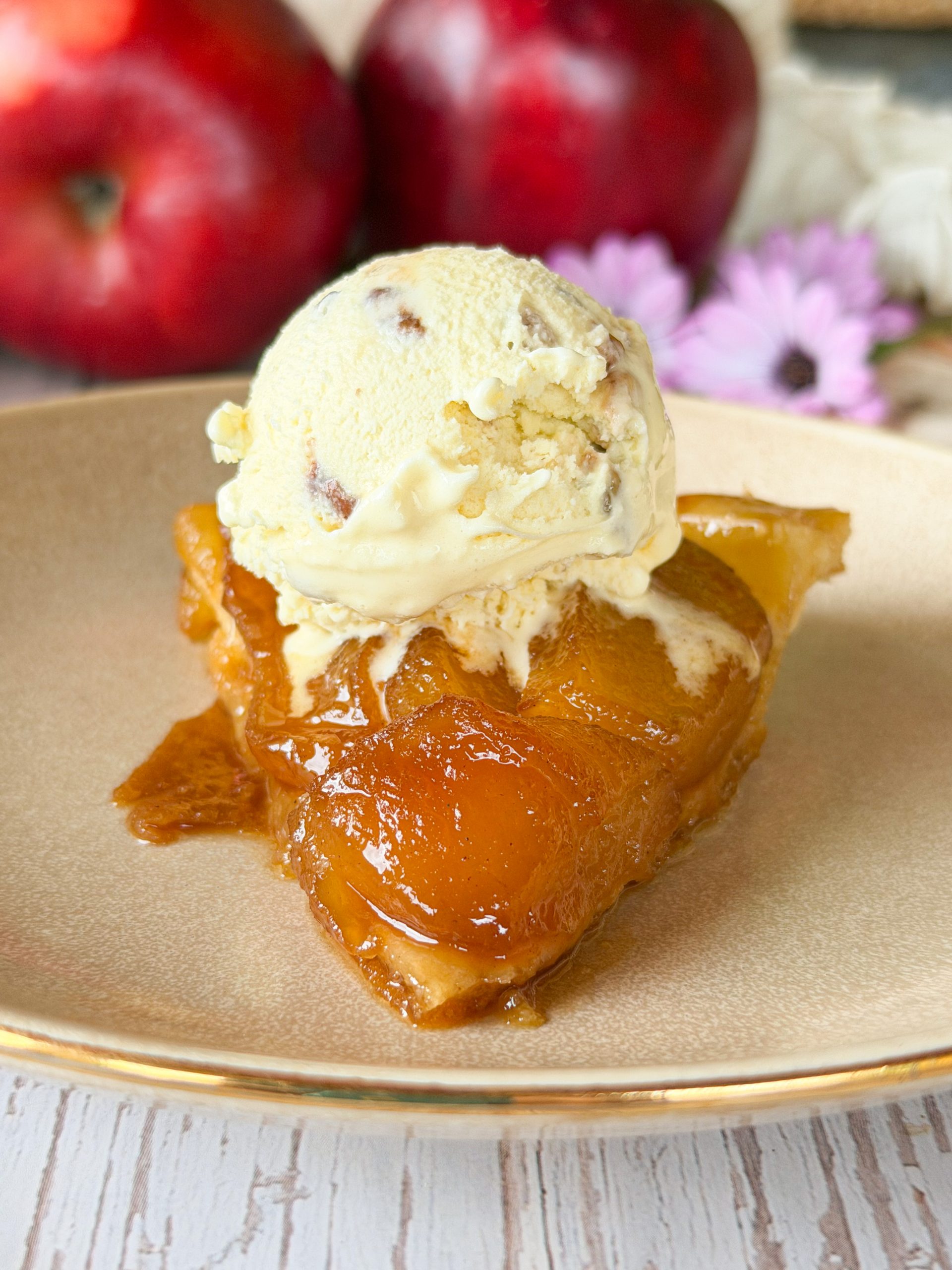 Primer plano de una porción de tarta Tatin tibia servida con una bola cremosa de helado de vainilla fundiéndose sobre el caramelo brillante.