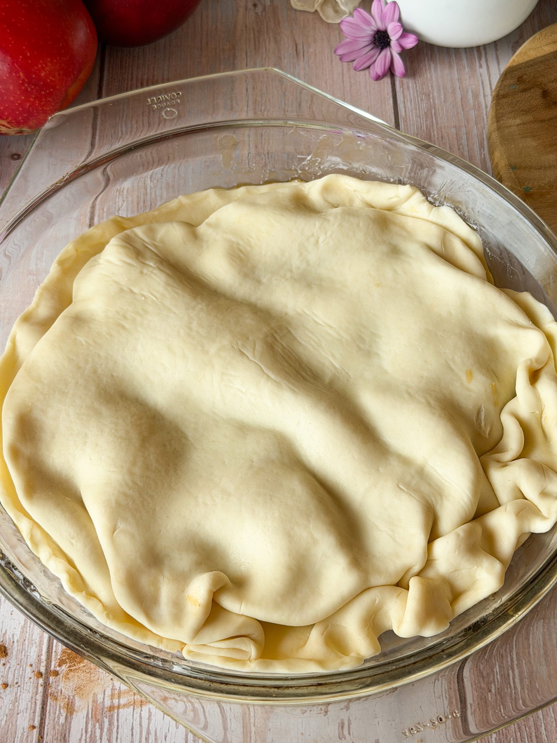 Molde de cristal con la masa de hojaldre cubriendo las manzanas, con los bordes metidos hacia dentro de forma artesanal antes de entrar al horno.