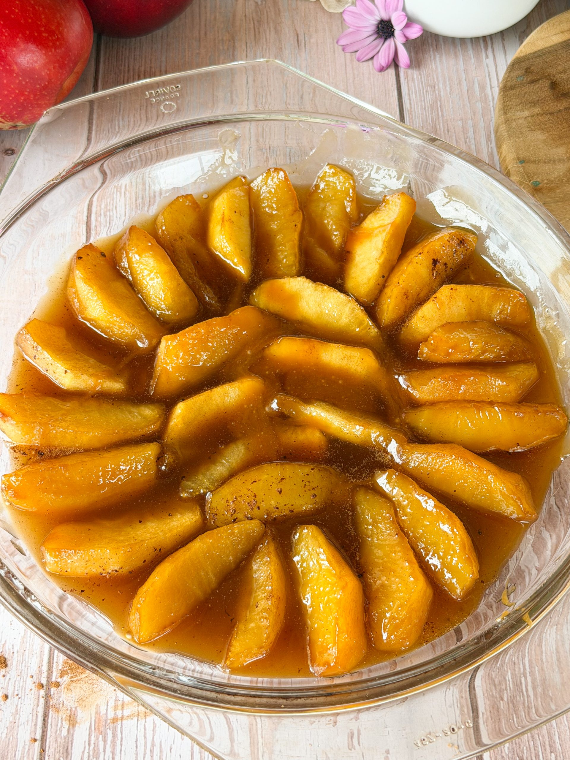 Disposición circular de gajos de manzana caramelizados cubriendo el fondo de un molde de cristal, bañados en una salsa de caramelo y mantequilla.