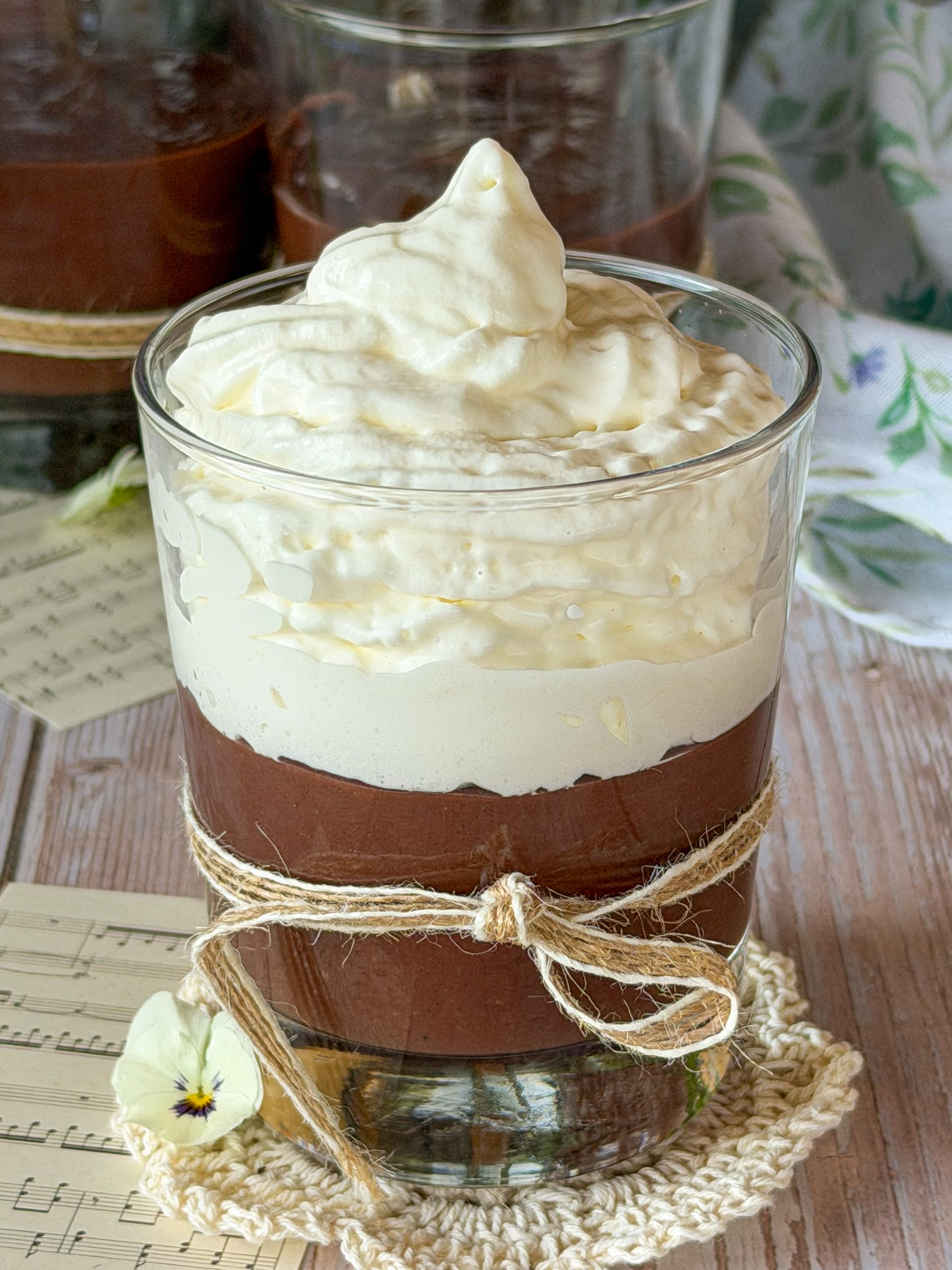 Copa de cristal rellena de crema de chocolate casera y coronada con una generosa nube de nata montada artesanal, sobre un fondo cálido.