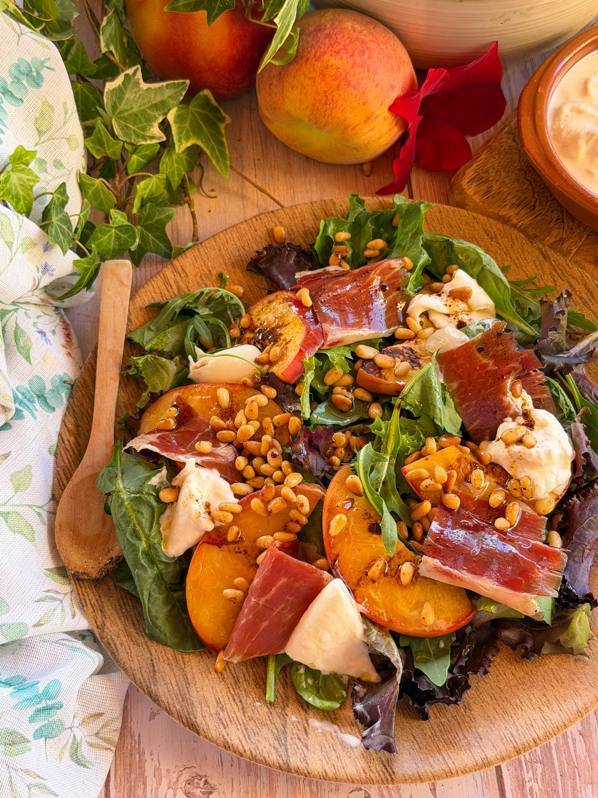 Plato de ensalada de verano con gajos de melocotón templado caramelizado, burrata fresca y jamón ibérico, espolvoreado con piñones tostados