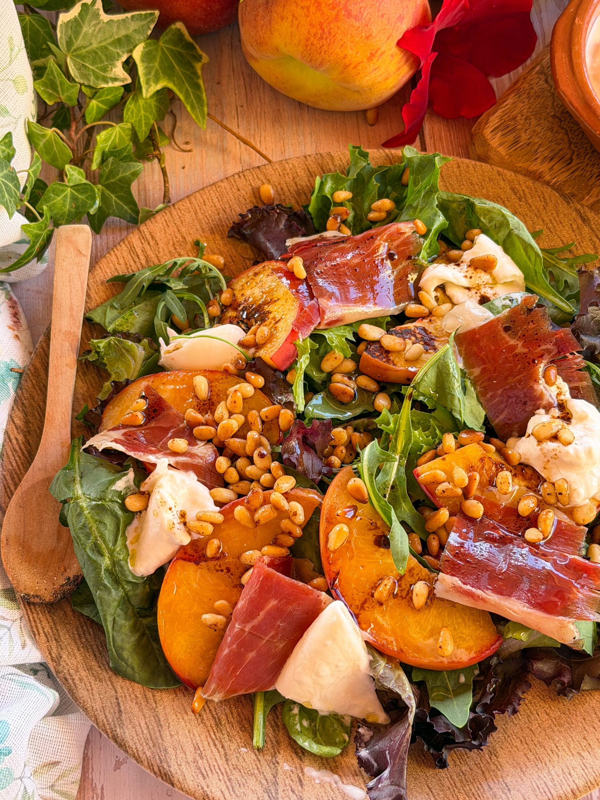 Plato de ensalada de verano con gajos de melocotón templado caramelizado, burrata fresca y jamón ibérico, espolvoreado con piñones tostados