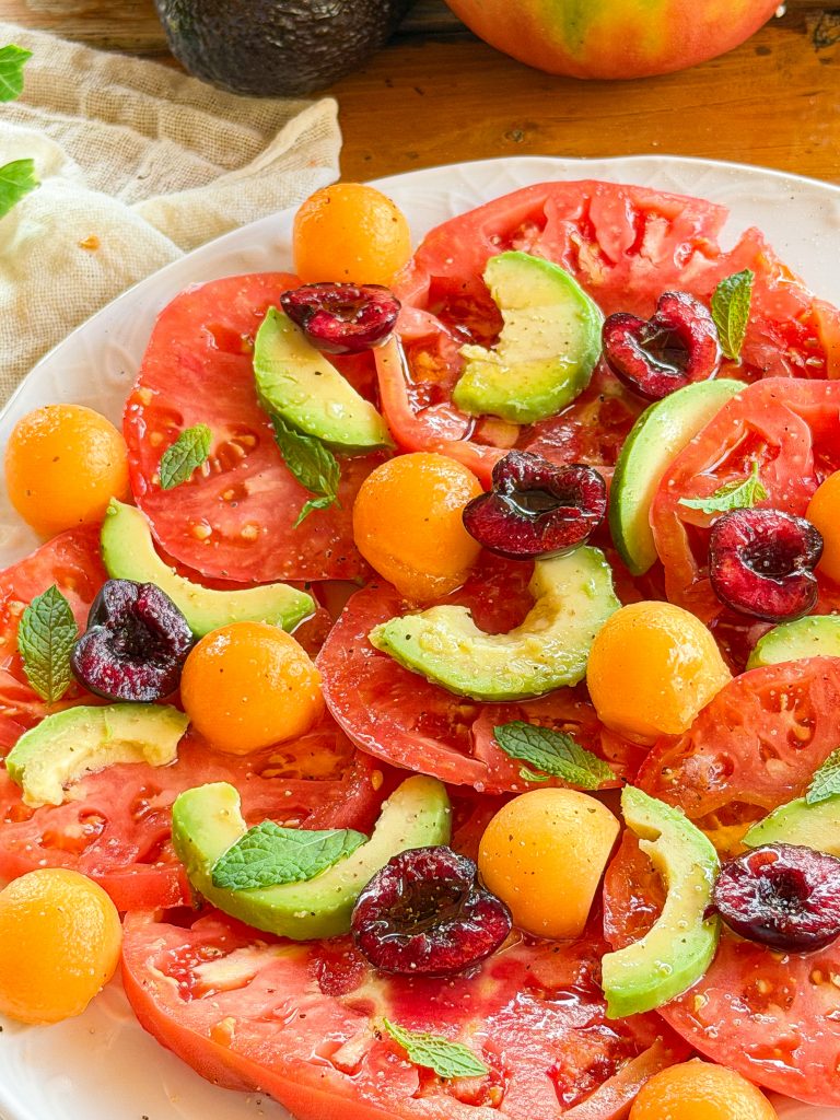 Ensalada de tomate rosa con aguacate, melón cantalupo, cerezas y hojas de menta fresca aliñada con aceite de oliva virgen extra.
