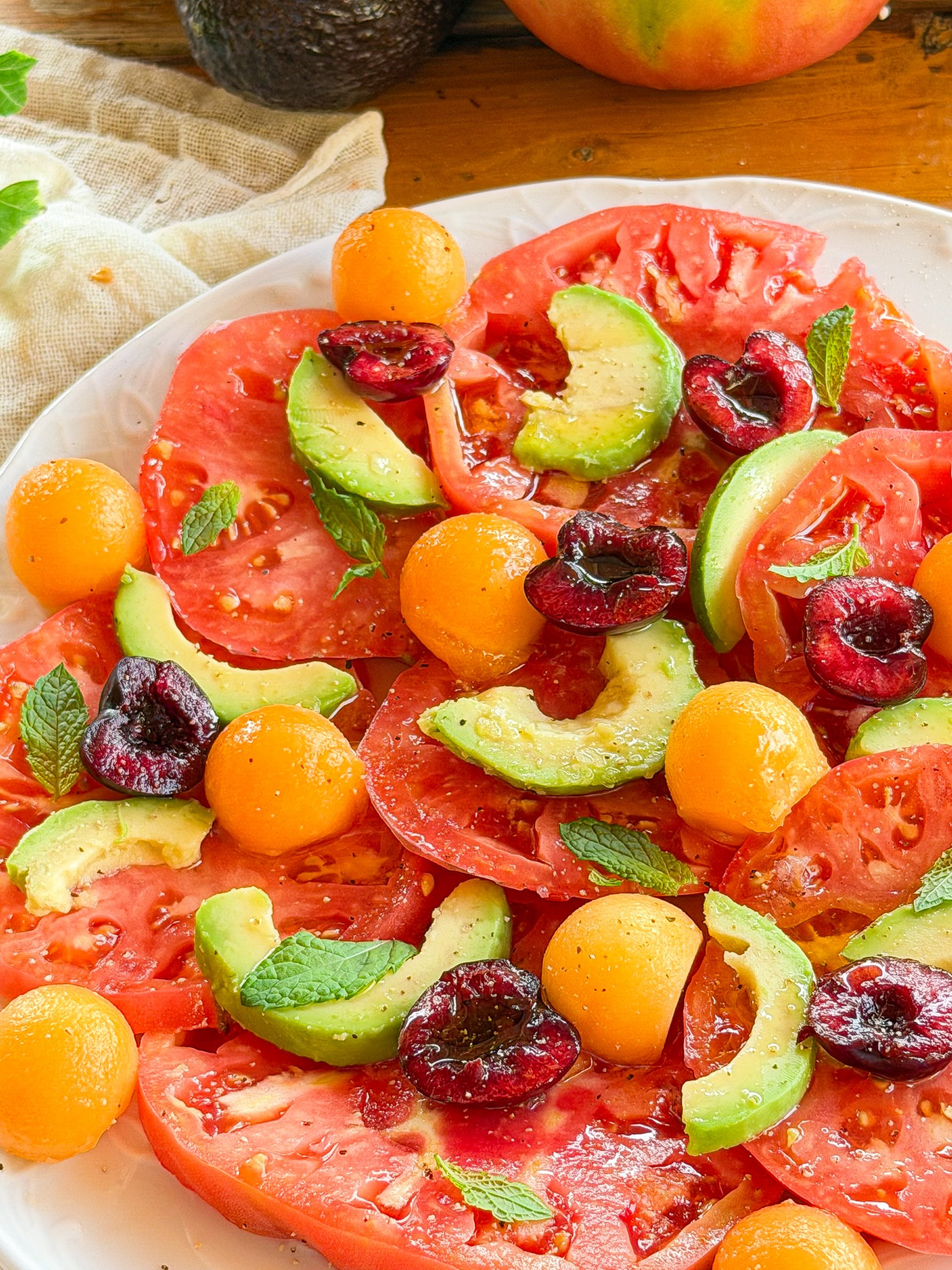 Ensalada de tomate rosa con aguacate, melón cantalupo, cerezas y hojas de menta fresca aliñada con aceite de oliva virgen extra.