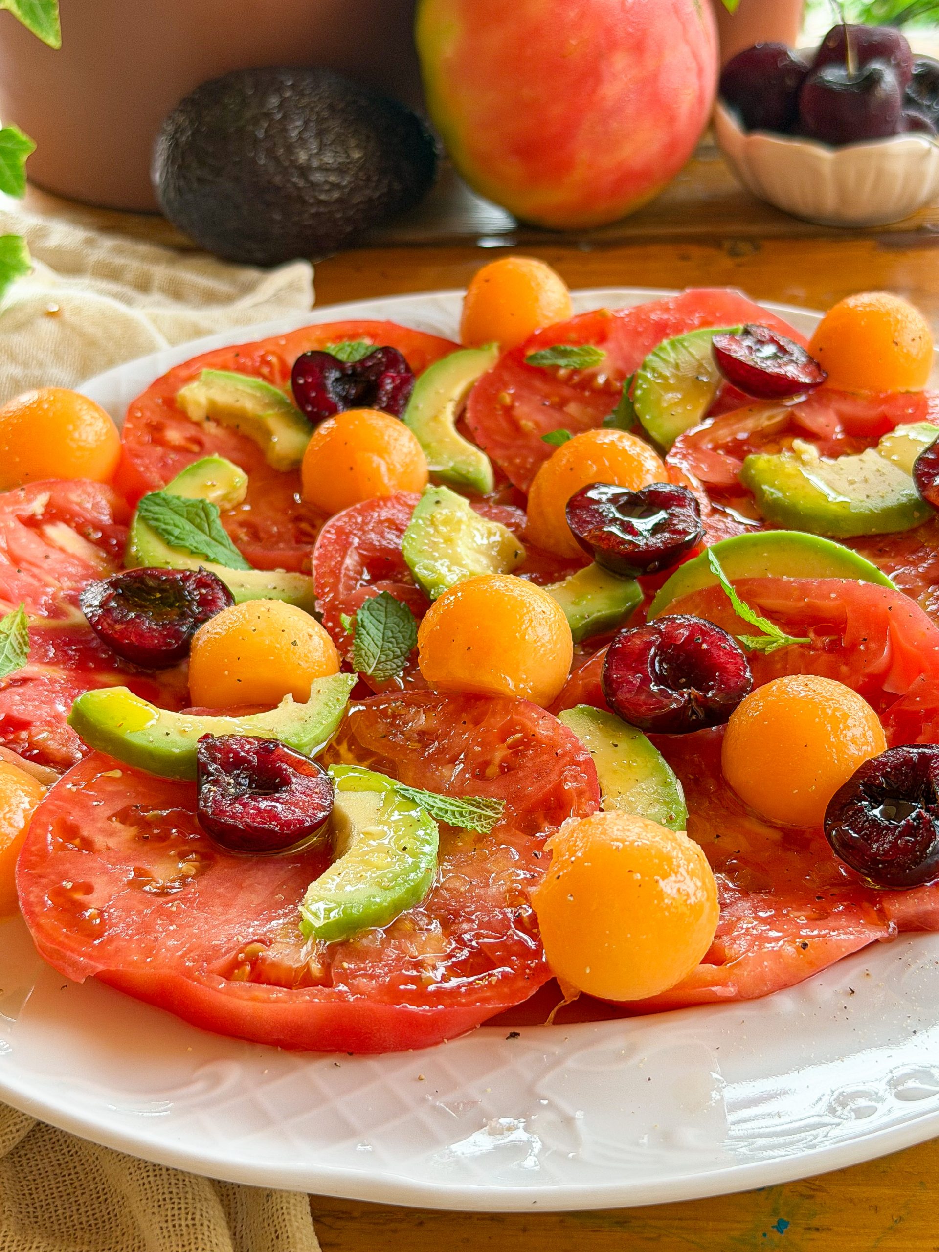 Ensalada de tomate rosa con aguacate, melón cantalupo, cerezas y hojas de menta fresca aliñada con aceite de oliva virgen extra.