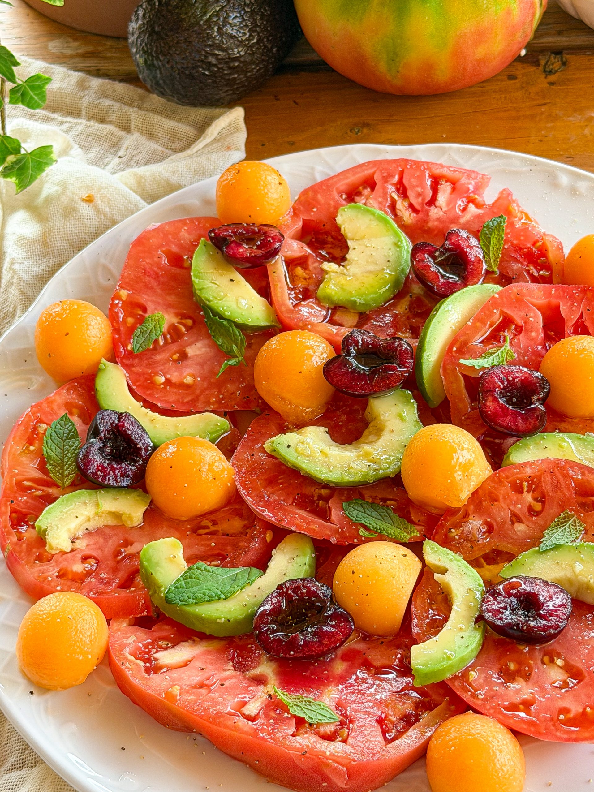 Ensalada de tomate rosa con aguacate, melón cantalupo, cerezas y hojas de menta fresca aliñada con aceite de oliva virgen extra.