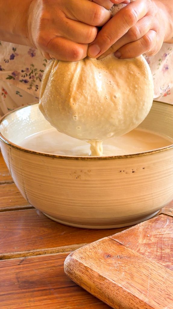 Manos exprimiendo una bolsa de tela sobre un bol de cerámica para filtrar horchata de chufa casera recién hecha.