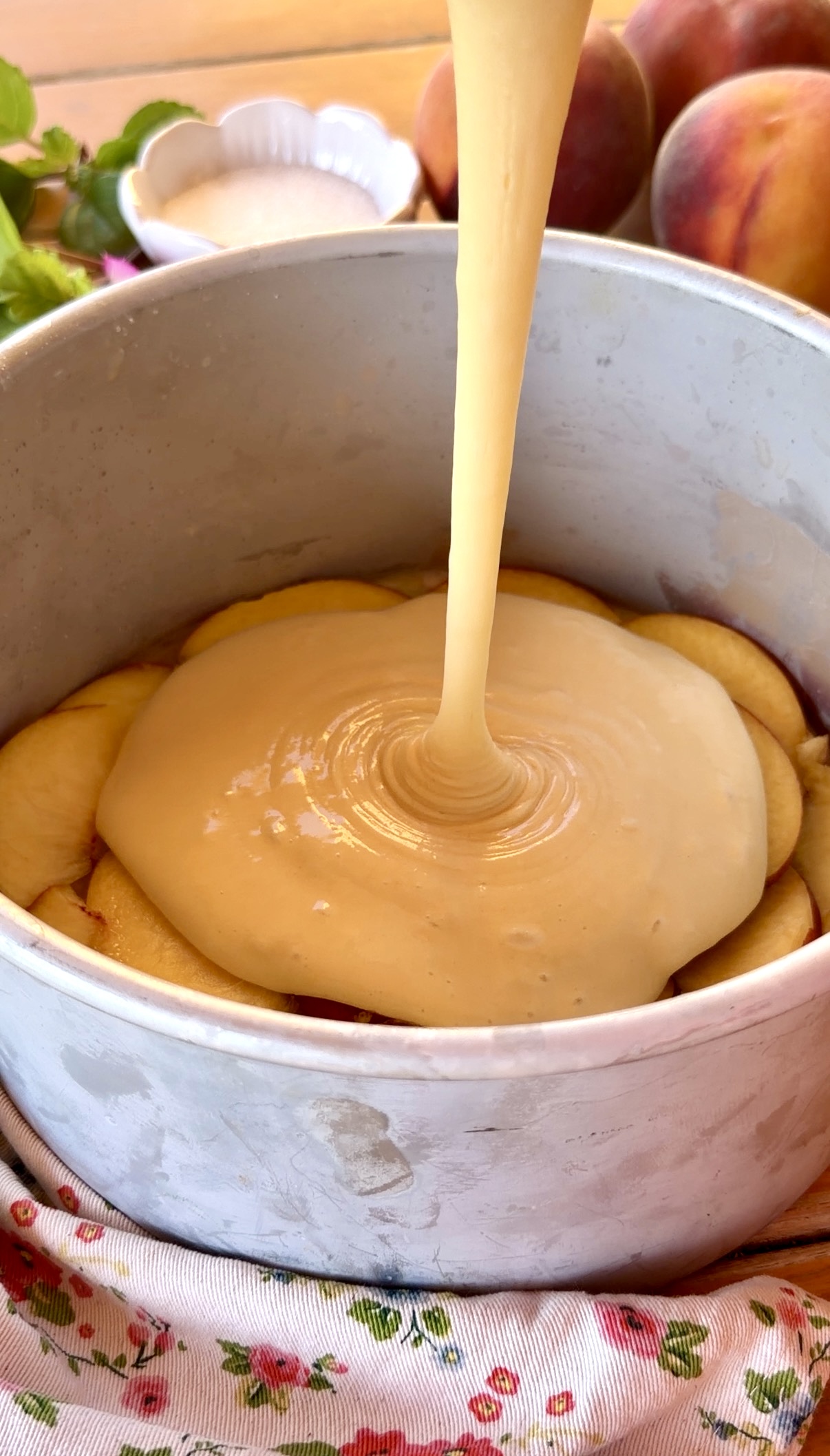 Masa de bizcocho cayendo sobre una base de melocotones caramelizados en un molde redondo antes del horneado.