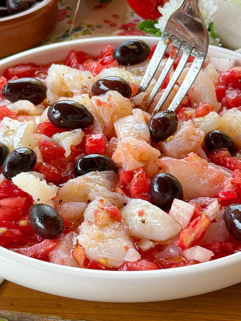 Esqueixada de bacalao catalana casera elaborada con tomate maduro, cebolla, aceitunas negras y bacalao desalado, una receta fresca típica del verano.