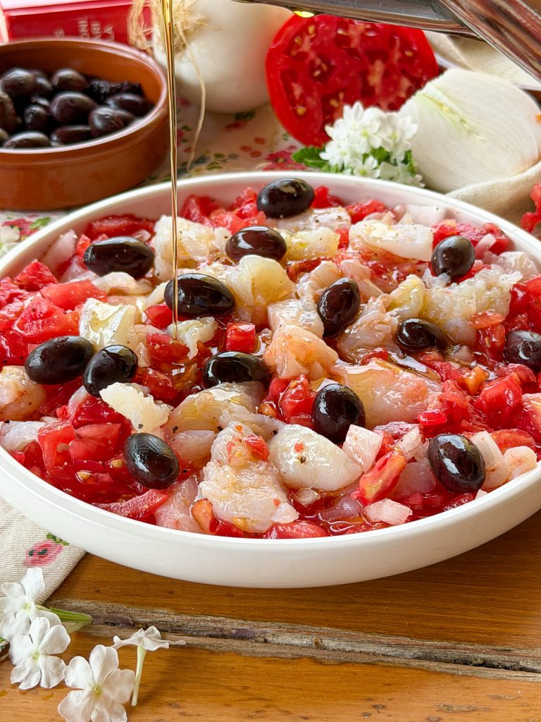 Esqueixada de bacalao catalana casera elaborada con tomate maduro, cebolla, aceitunas negras y bacalao desalado, una receta fresca típica del verano.