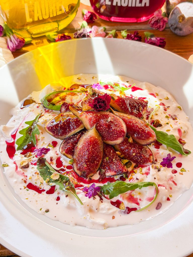 Higos salteados con burrata cremosa, pistachos y aceite de oliva rosa servidos en un plato blanco.