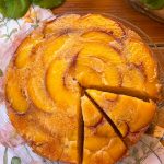 Bizcocho invertido de melocotón caramelizado recién horneado, con una porción servida y la superficie brillante de fruta caramelizada.