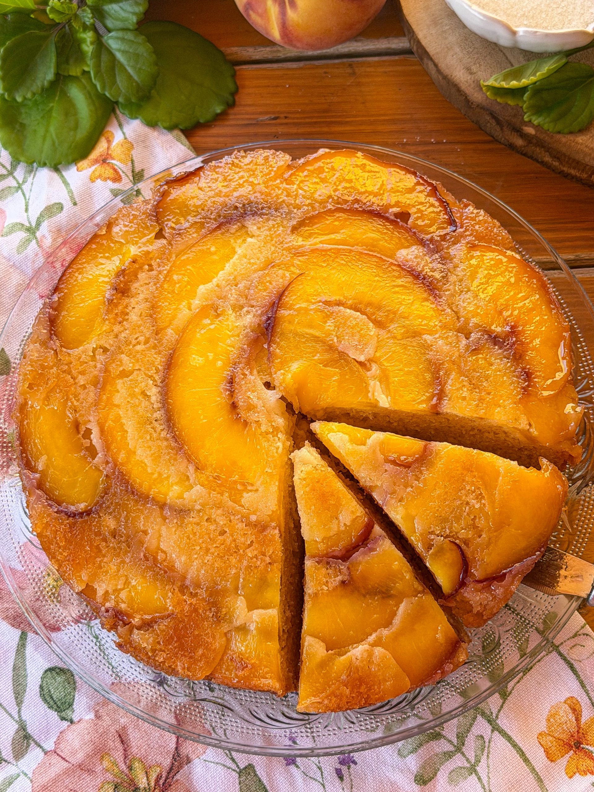 Bizcocho invertido de melocotón caramelizado recién horneado, con una porción servida y la superficie brillante de fruta caramelizada.
