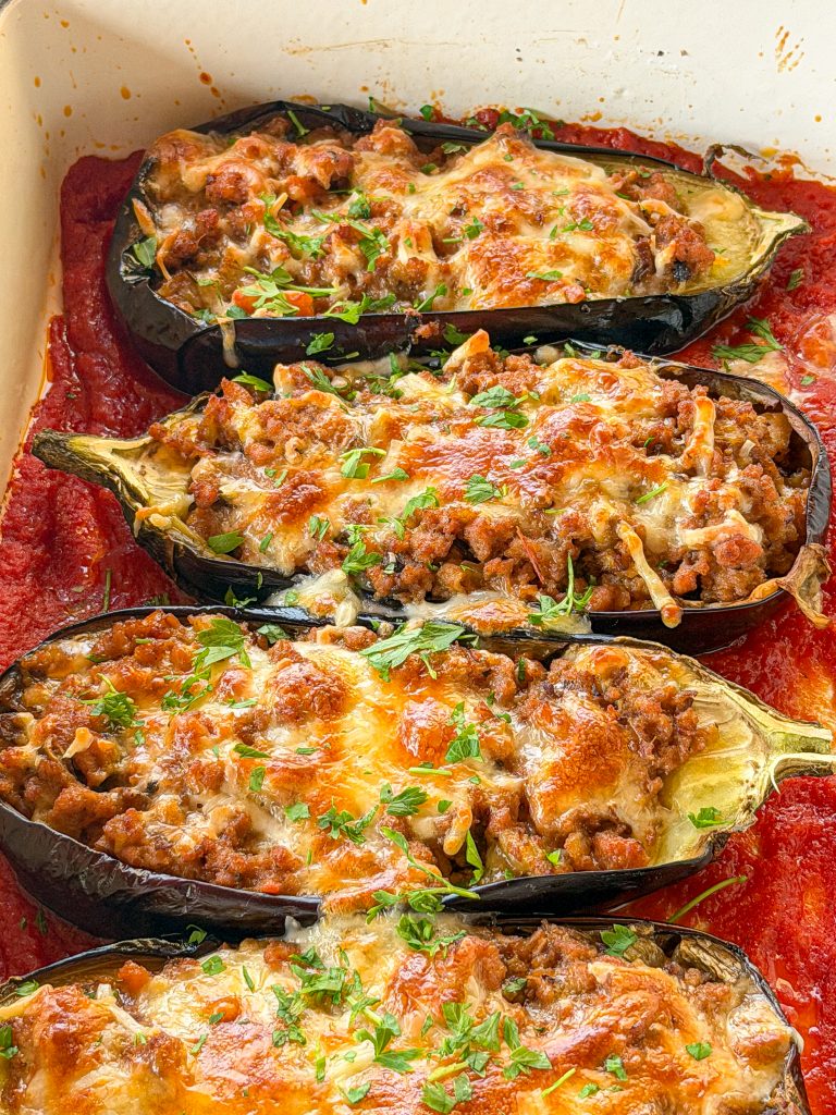 Berenjenas rellenas de carne al horno gratinadas con queso fundido en bandeja de horno sobre salsa de tomate casera.
