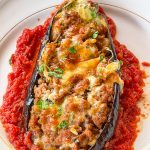 Berenjena rellena de carne al horno gratinada con mozzarella sobre una base de tomate casero y perejil fresco.