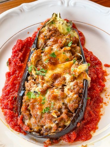 Berenjena rellena de carne al horno gratinada con mozzarella sobre una base de tomate casero y perejil fresco.