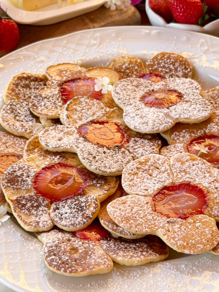 Plato lleno de tortitas caseras con rodajas de fresa en el centro, espolvoreadas con azúcar glass.