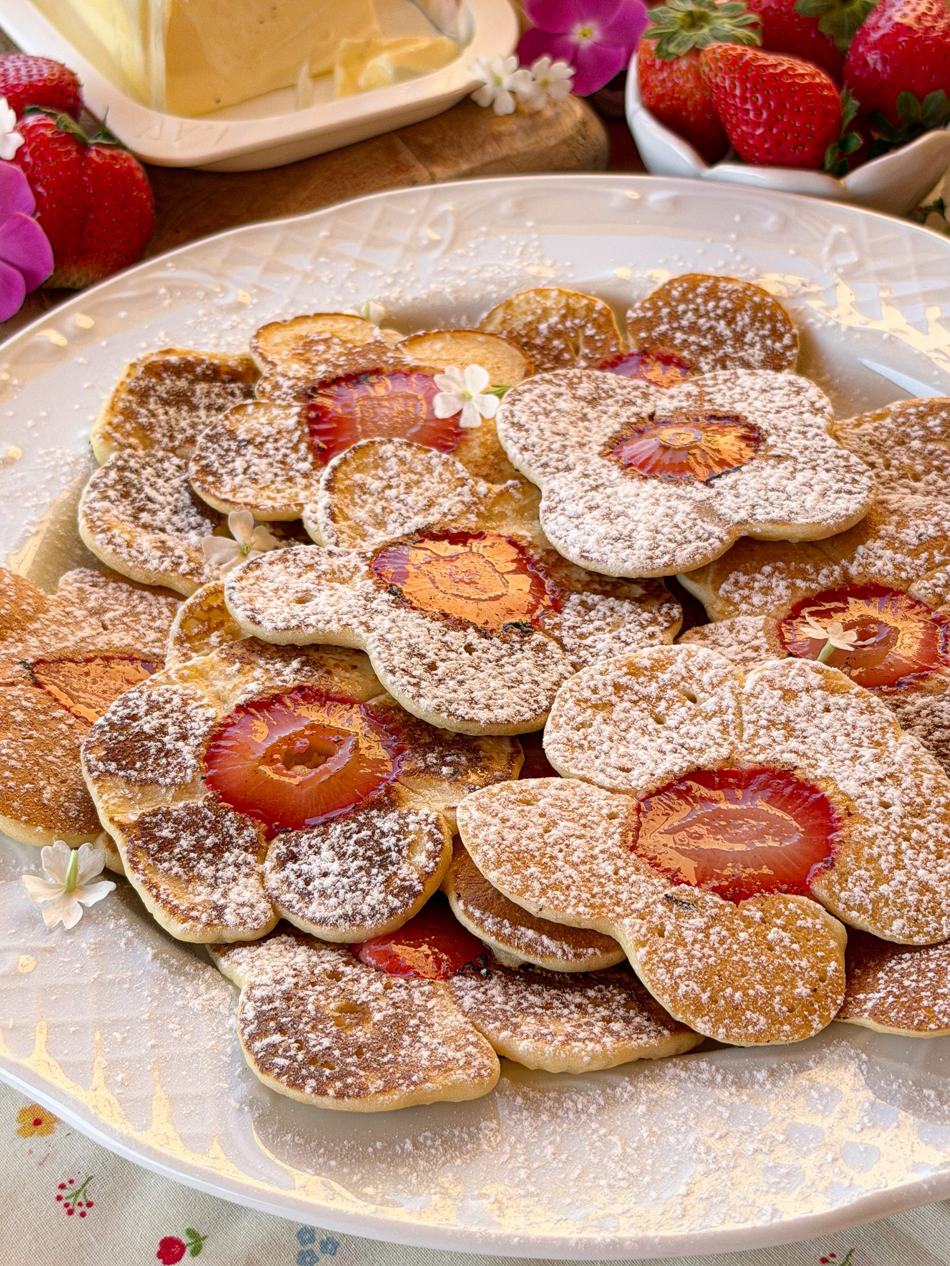 Plato lleno de tortitas caseras con rodajas de fresa en el centro, espolvoreadas con azúcar glass.