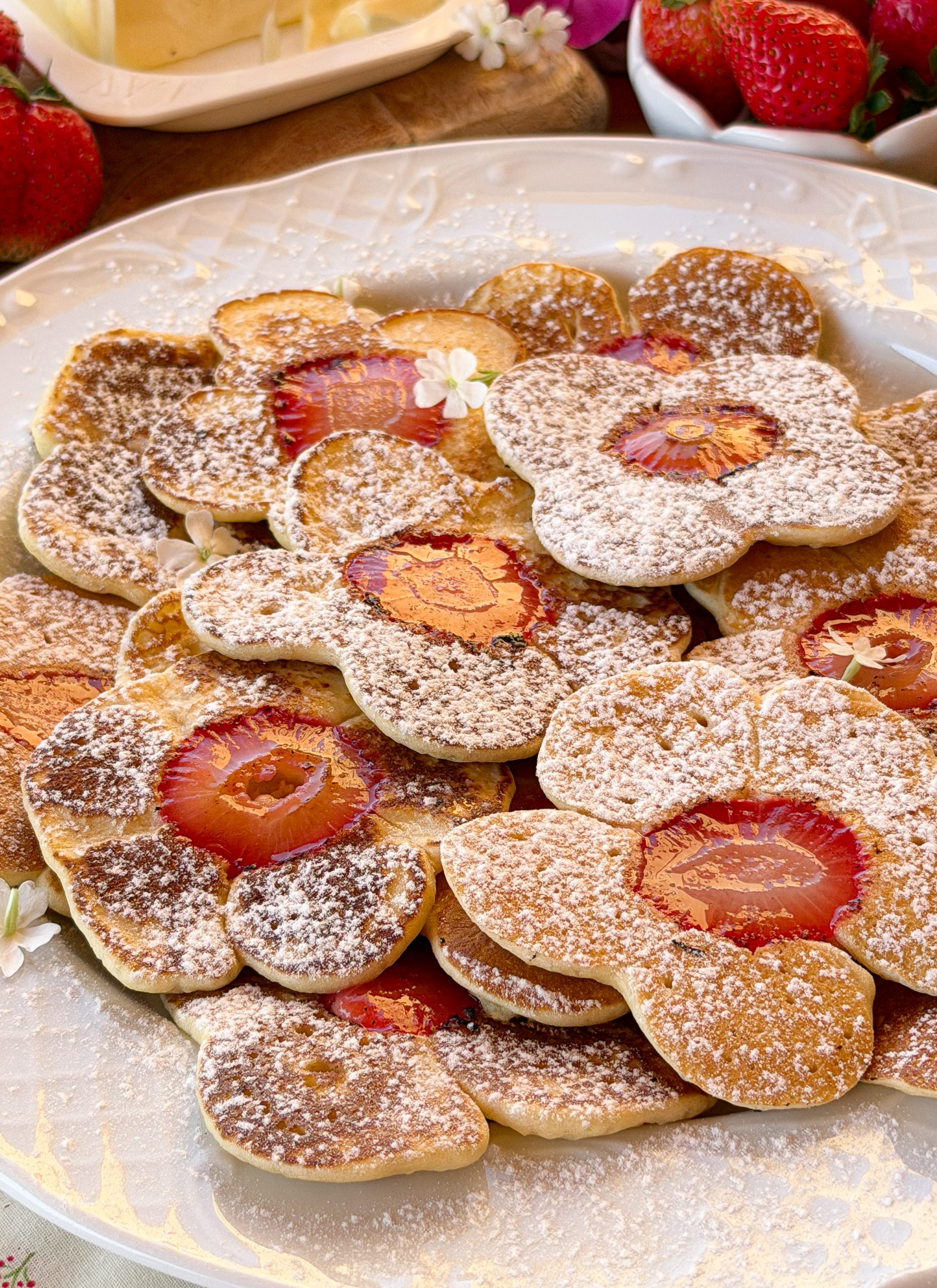 Plato lleno de tortitas caseras con rodajas de fresa en el centro, espolvoreadas con azúcar glass.