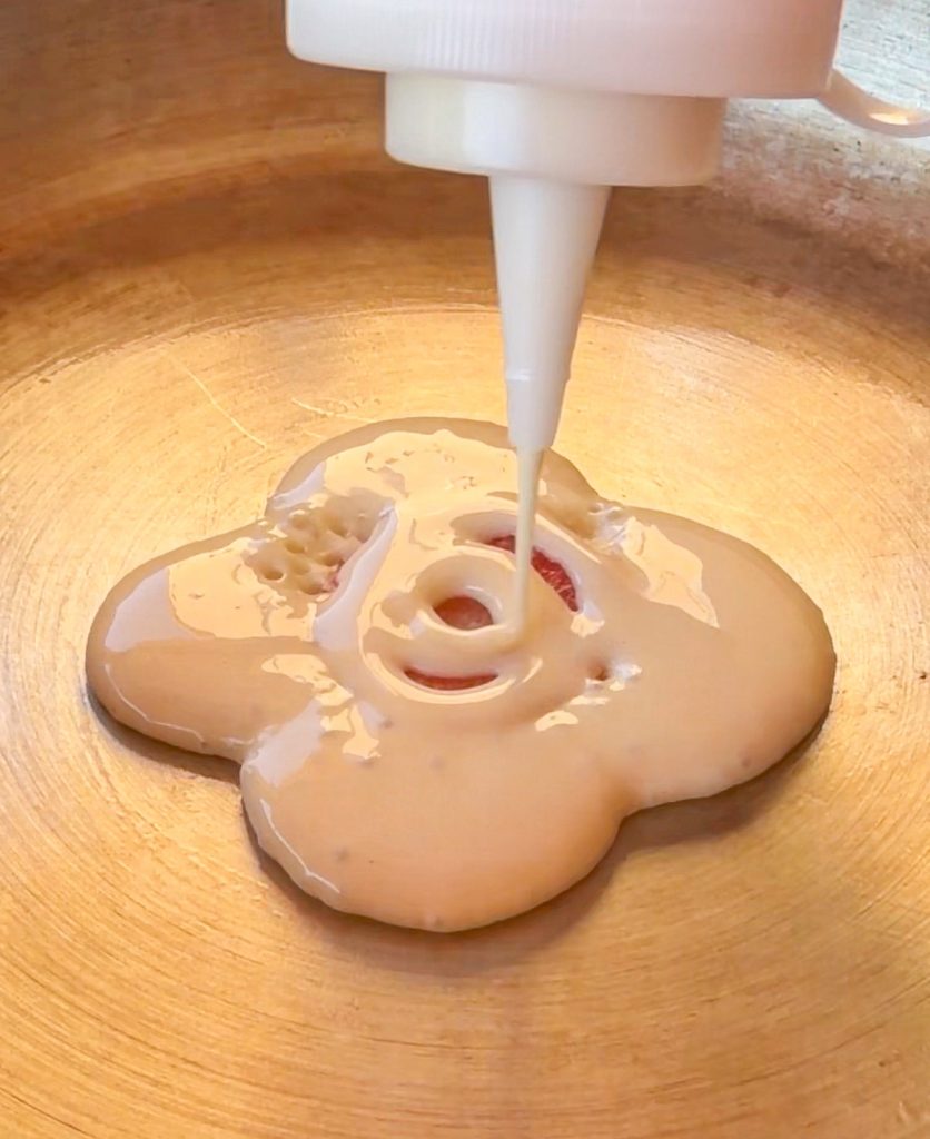 Rodaja de fresa fresca en el centro de una sartén con el comienzo de la masa de tortita vertida alrededor.