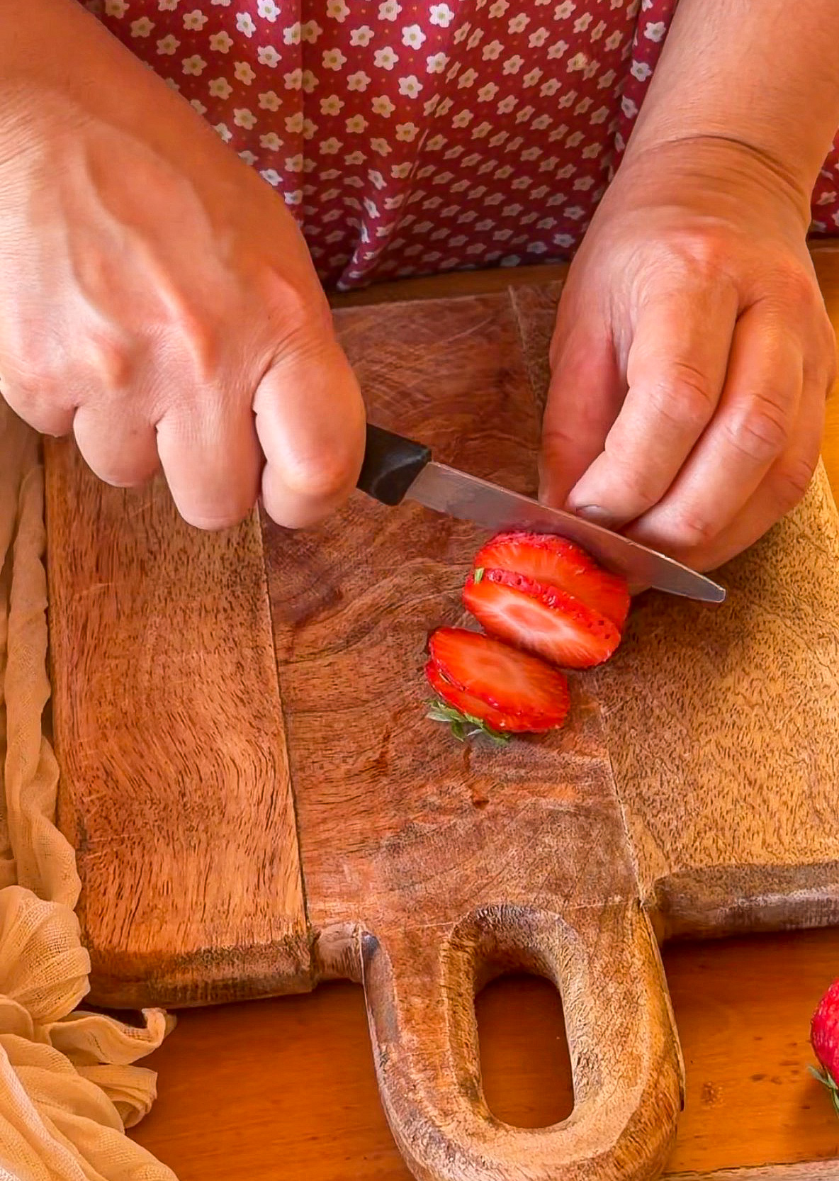 Manos cortando rodajas de fresa fresca sobre una tabla de madera con un cuchillo.