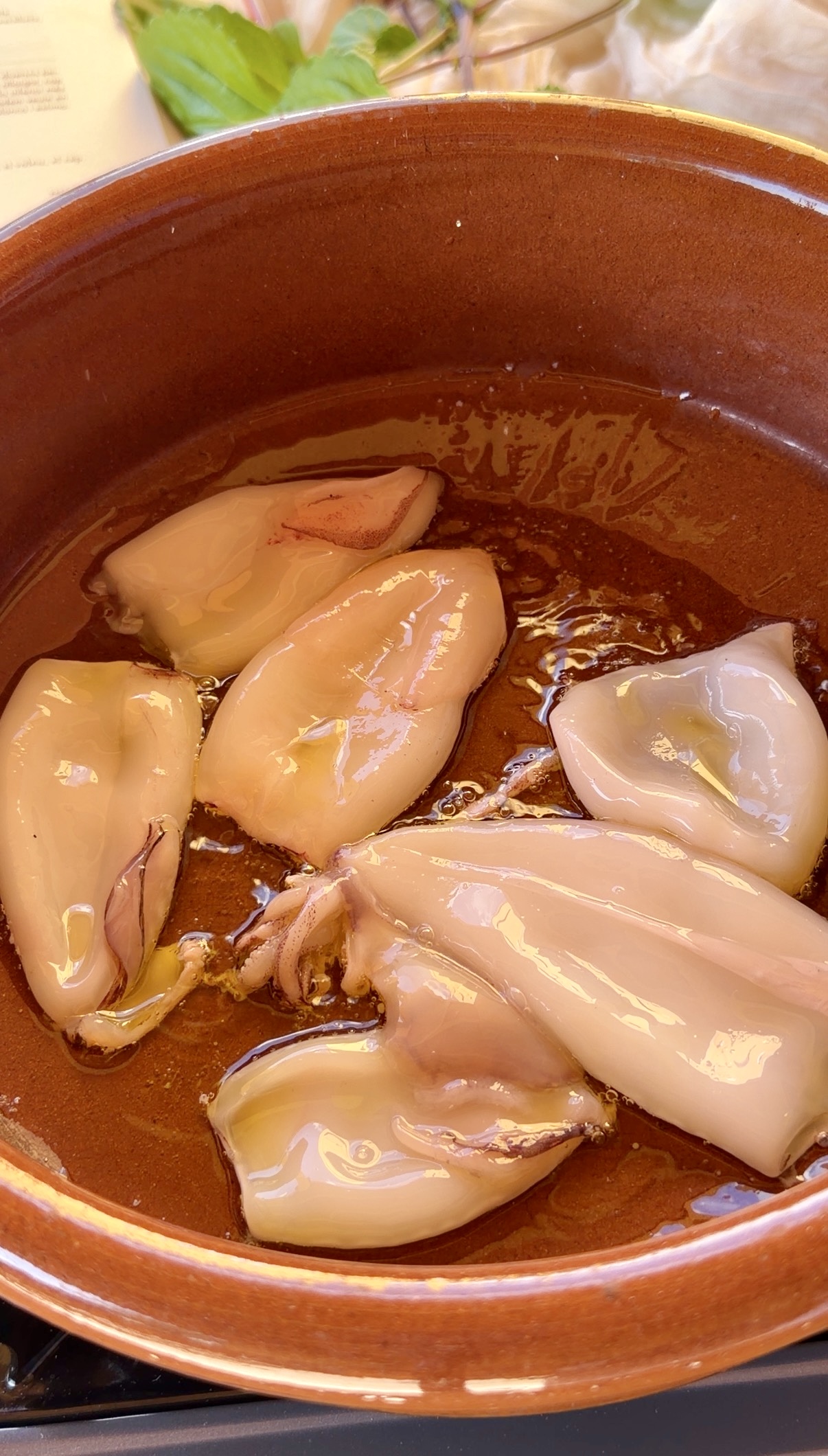 Calamarcets dorándose en aceite de oliva dentro de una cazuela de barro para preparar un suquet de peix tradicional.