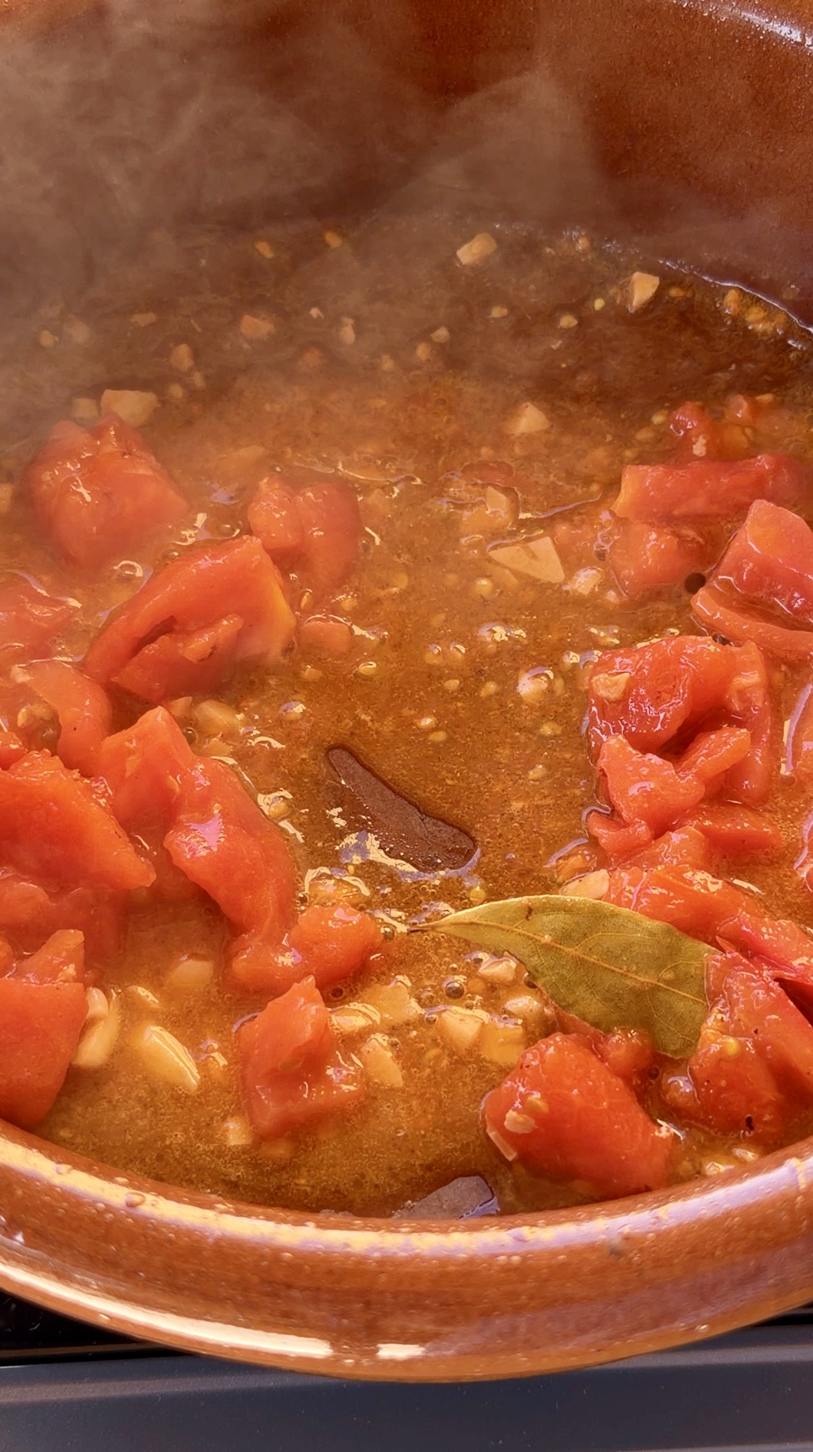 Sofrito de ajo picado, tomate pelado y hoja de laurel cocinándose lentamente en una cazuela de barro.