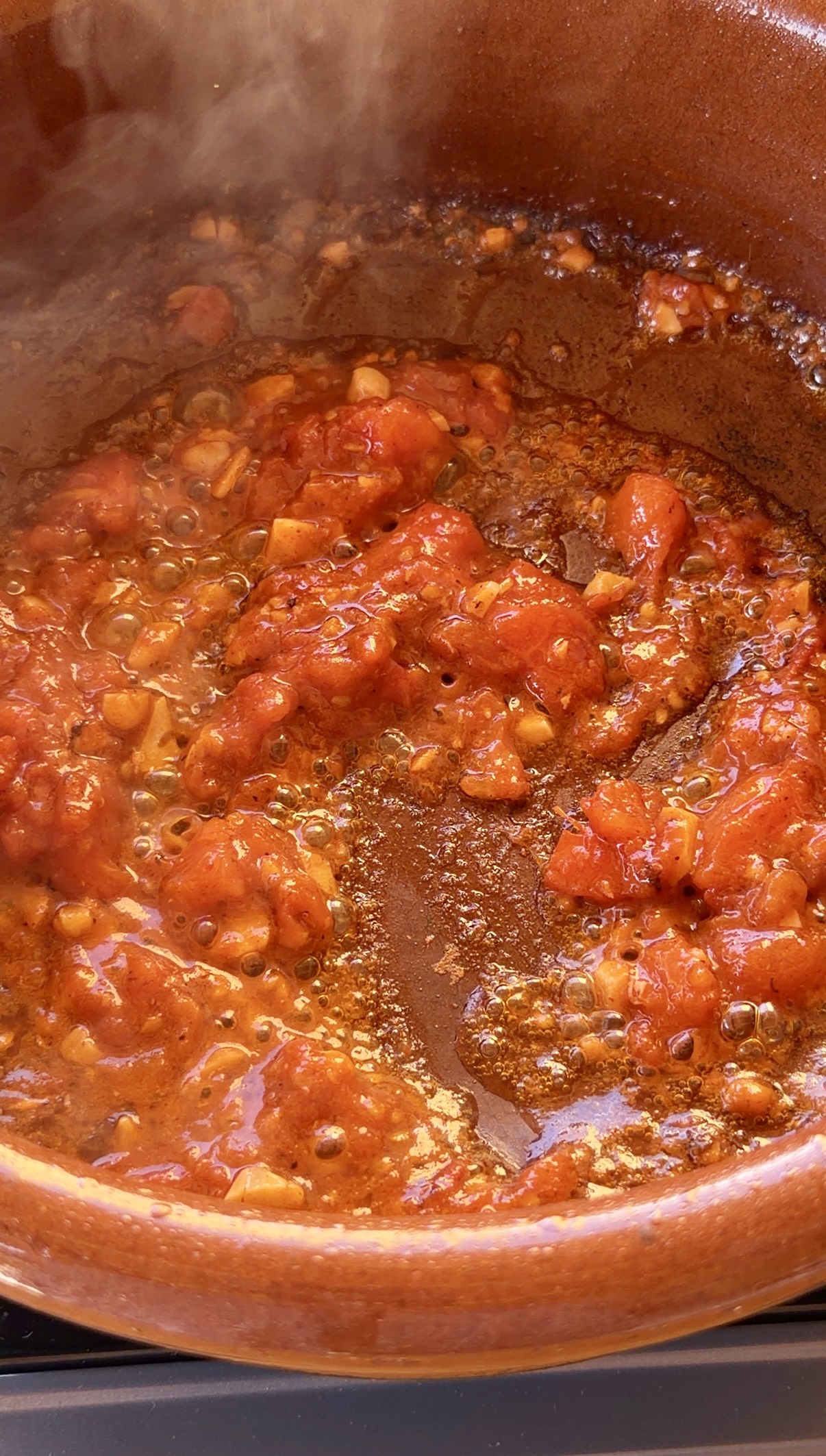 Sofrito de ajo picado, tomate pelado y hoja de laurel cocinándose lentamente en una cazuela de barro.