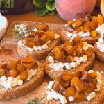 Tostadas con queso cottage y melocotón confitado sin azúcar, servidas sobre tabla de madera. Desayuno casero fácil con fruta de temporada.