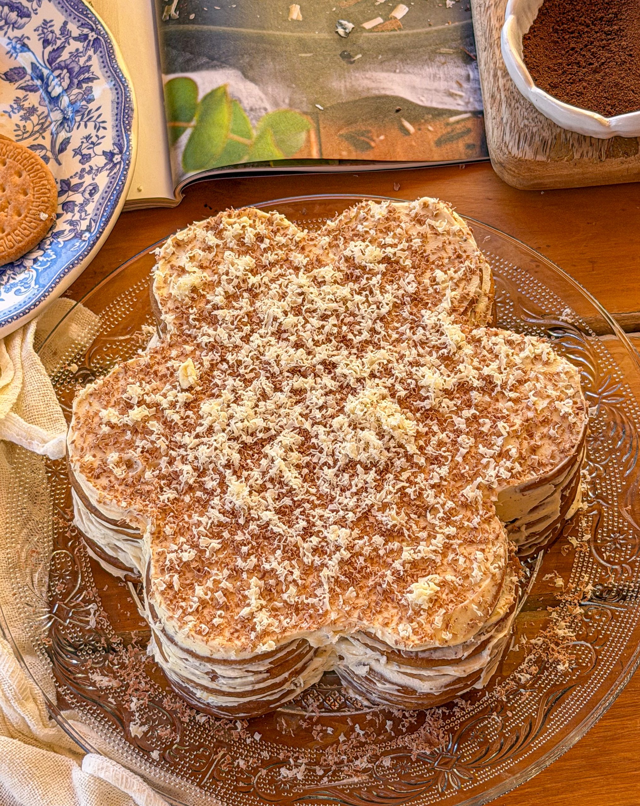 Tarta portuguesa de galletas en forma de flor, elaborada con capas de galletas María y crema de café, decorada con chocolate rallado blanco y negro sobre una bandeja de cristal.