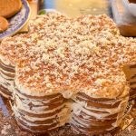 Tarta portuguesa de galletas en forma de flor, elaborada con capas de galletas María y crema de café, decorada con chocolate rallado blanco y negro sobre una bandeja de cristal.