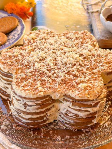 Tarta portuguesa de galletas en forma de flor, elaborada con capas de galletas María y crema de café, decorada con chocolate rallado blanco y negro sobre una bandeja de cristal.