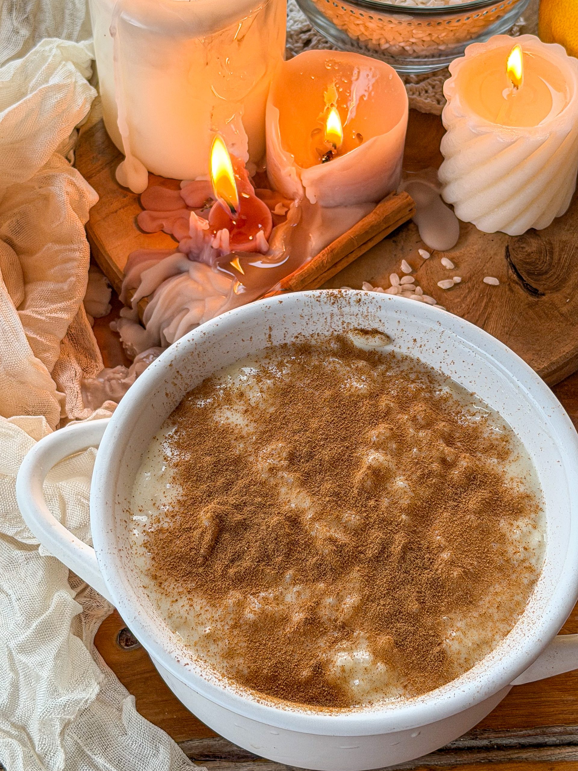 Arroz con leche casero espolvoreado con canela, presentado en un cuenco blanco con velas y arroz como decoración.