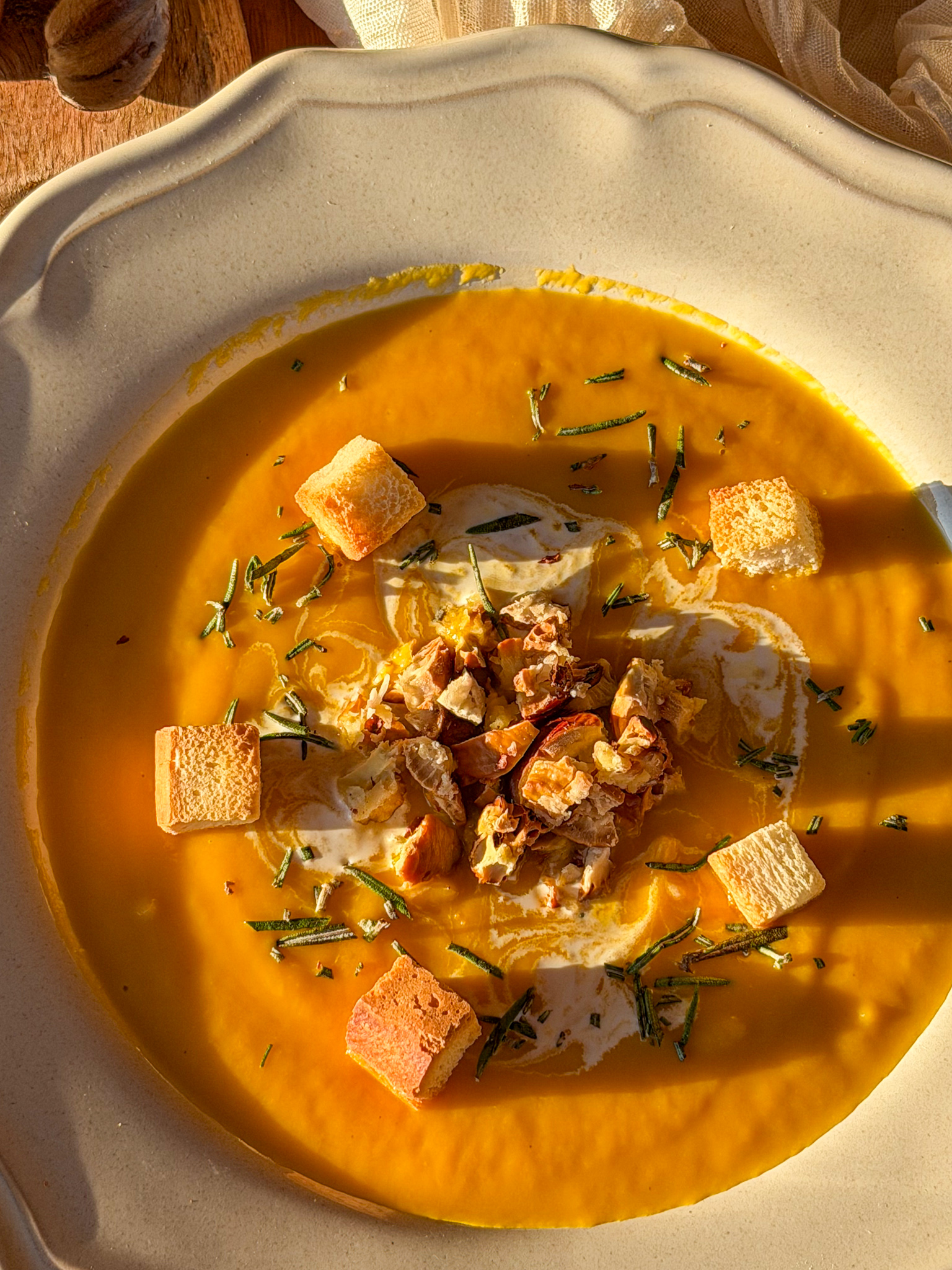 Crema de calabaza asada con castañas picadas, nata, romero fresco y picatostes de pan, servida en un plato rústico.