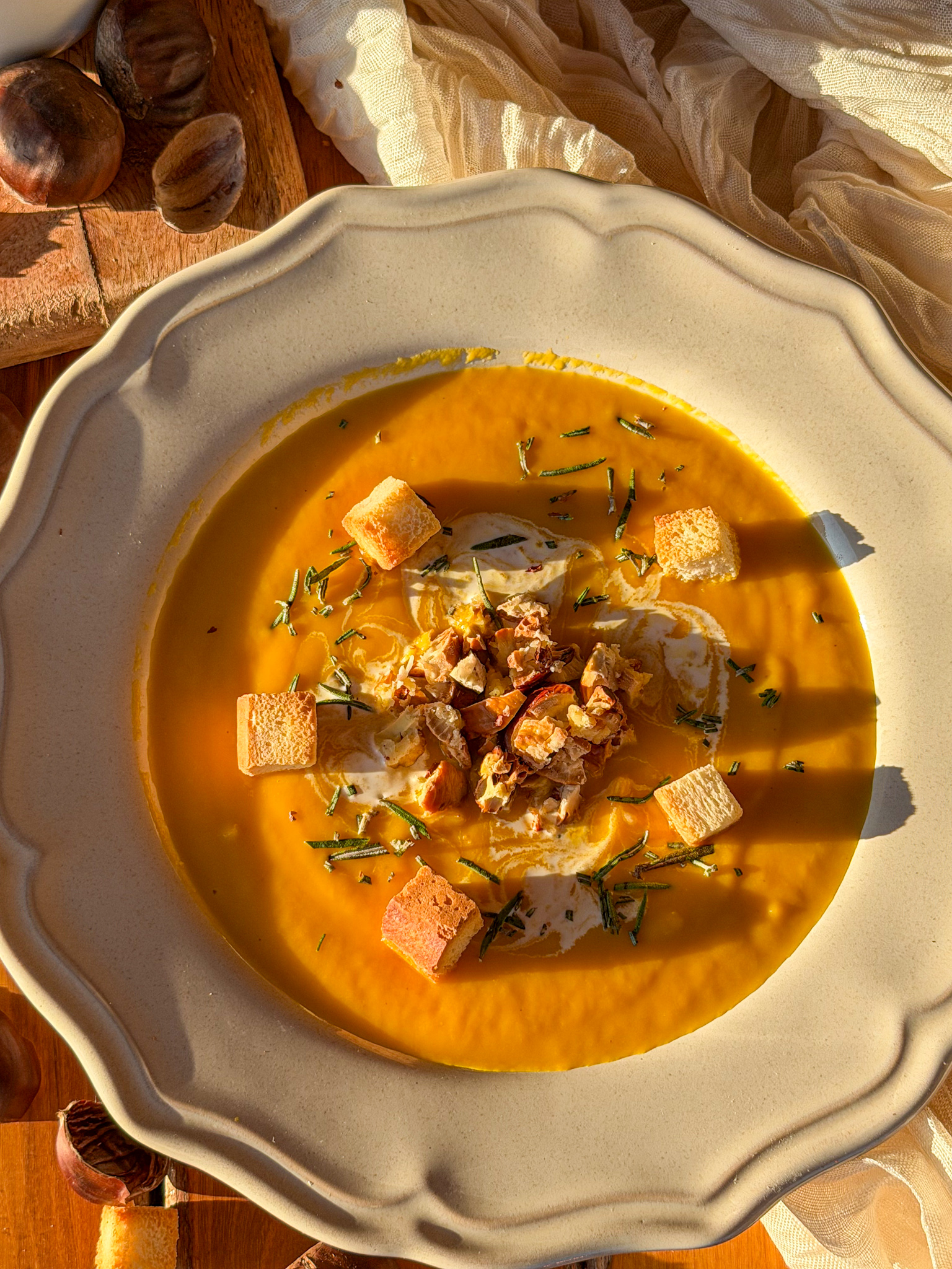 Crema de calabaza asada con castañas picadas, nata, romero fresco y picatostes de pan, servida en un plato rústico.
