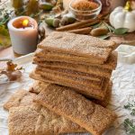 Galletas napolitanas caseras apiladas sobre papel de horno con decoración otoñal y canela en rama.