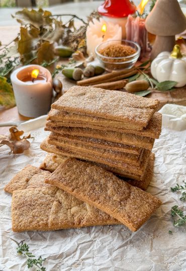 Galletas napolitanas caseras apiladas sobre papel de horno con decoración otoñal y canela en rama.