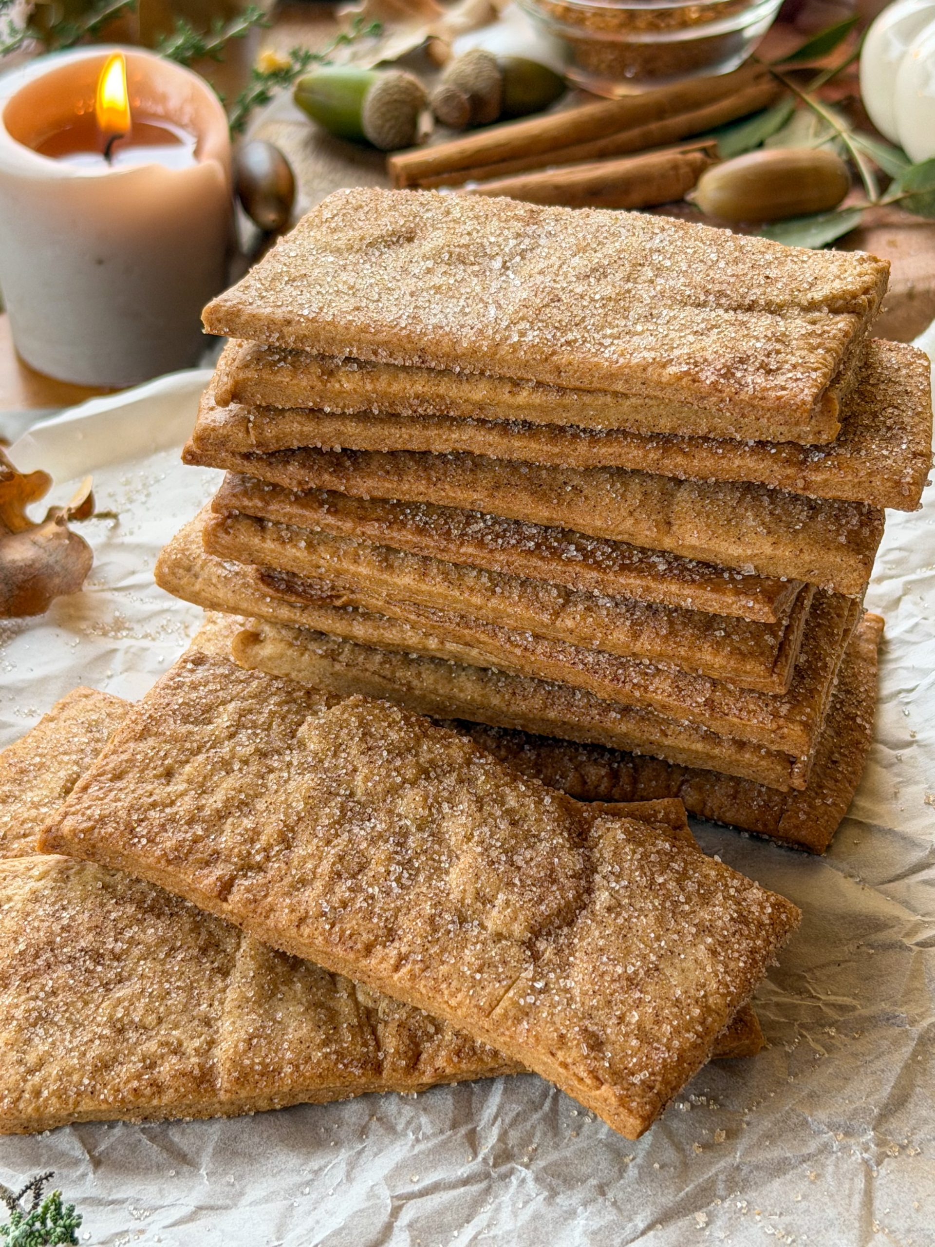 Galletas napolitanas caseras apiladas sobre papel de horno con decoración otoñal y canela en rama.