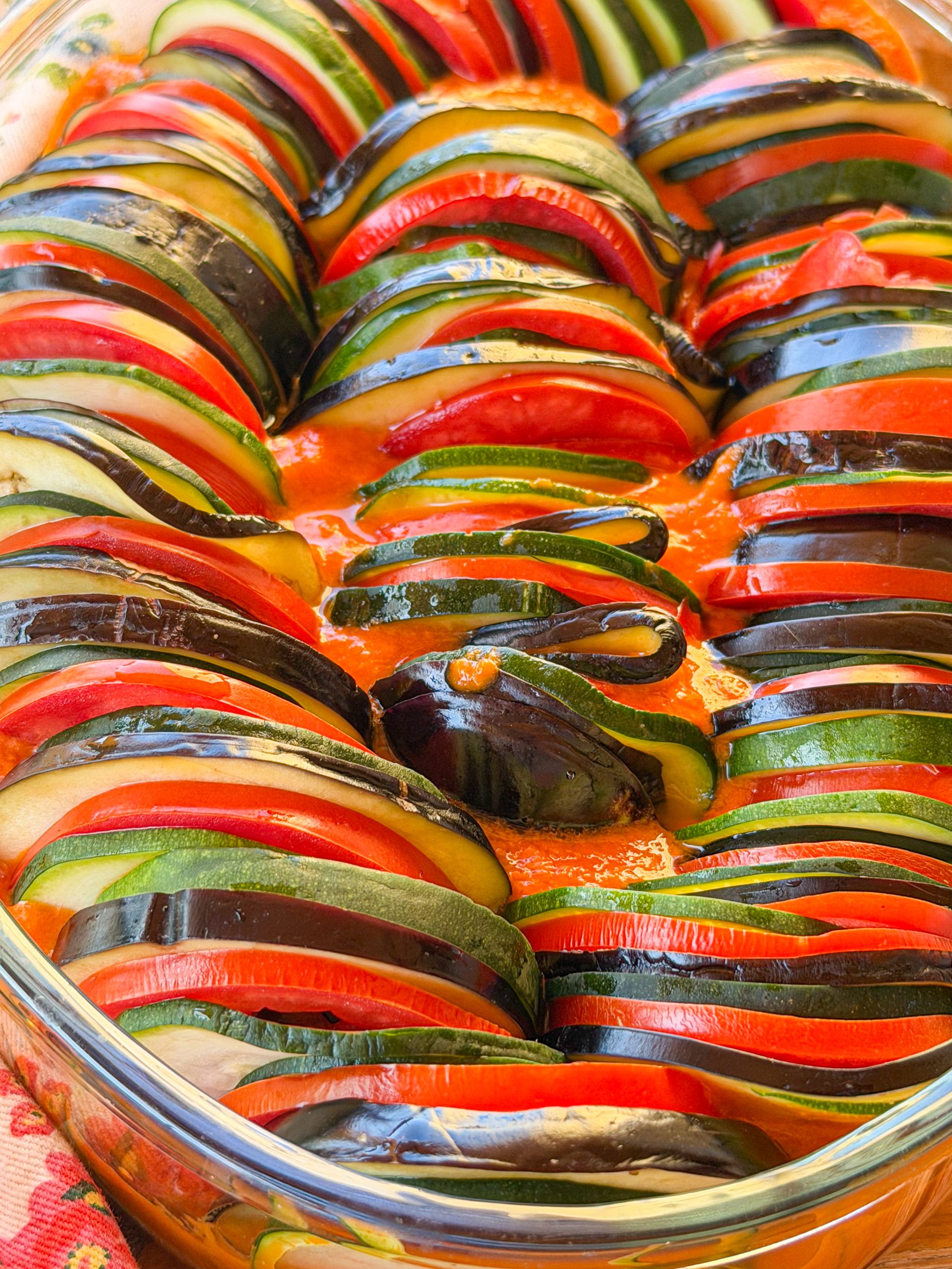 Ratatouille antes de hornear con rodajas de berenjena, calabacín y tomate colocadas sobre salsa de verduras.