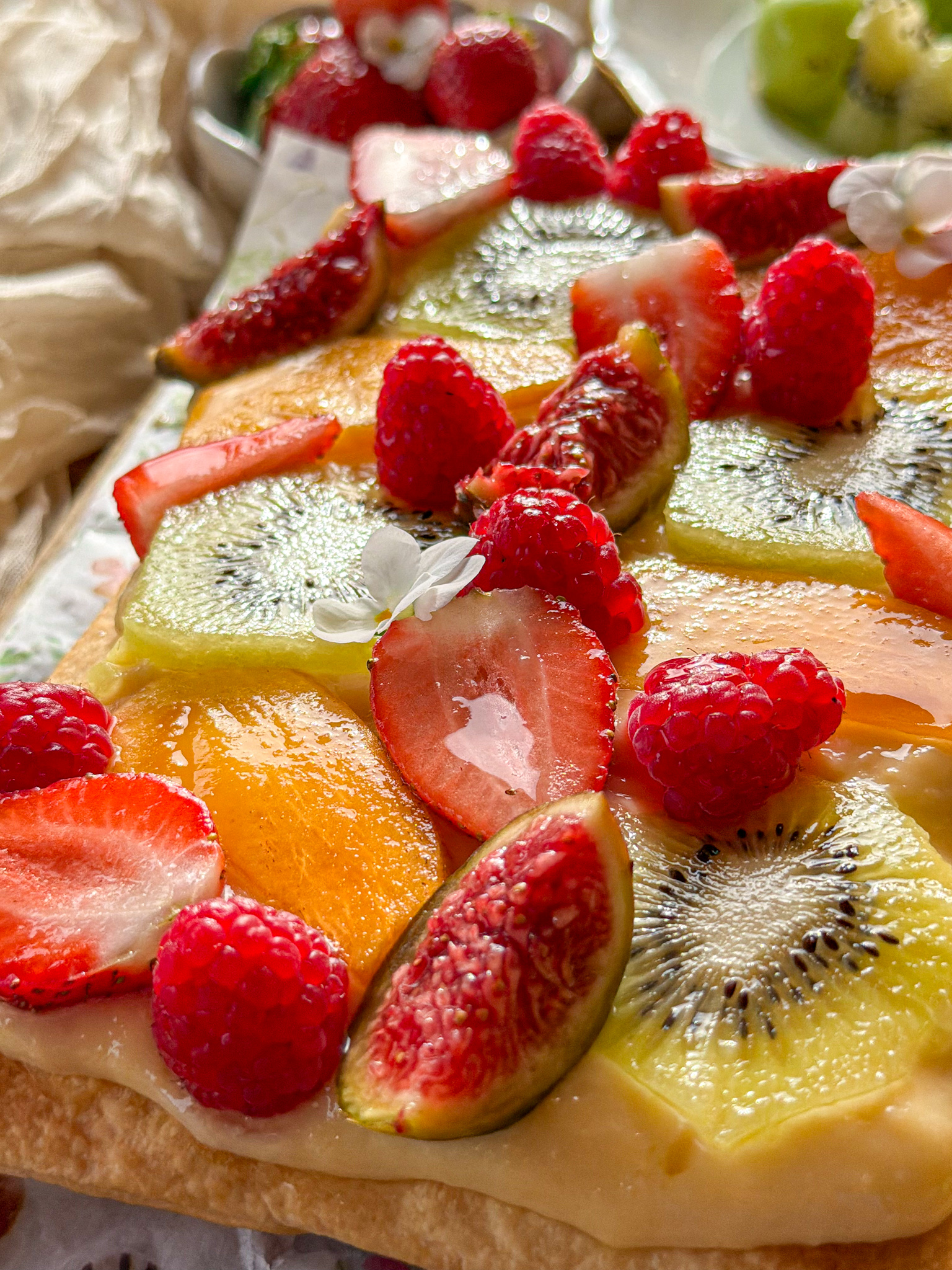 Tarta de frutas frescas con base de hojaldre crujiente y crema pastelera, decorada con kiwi, fresas, frambuesas, caqui e higos.