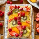Tarta de frutas frescas con base de hojaldre crujiente y crema pastelera, decorada con kiwi, fresas, frambuesas, caqui e higos.